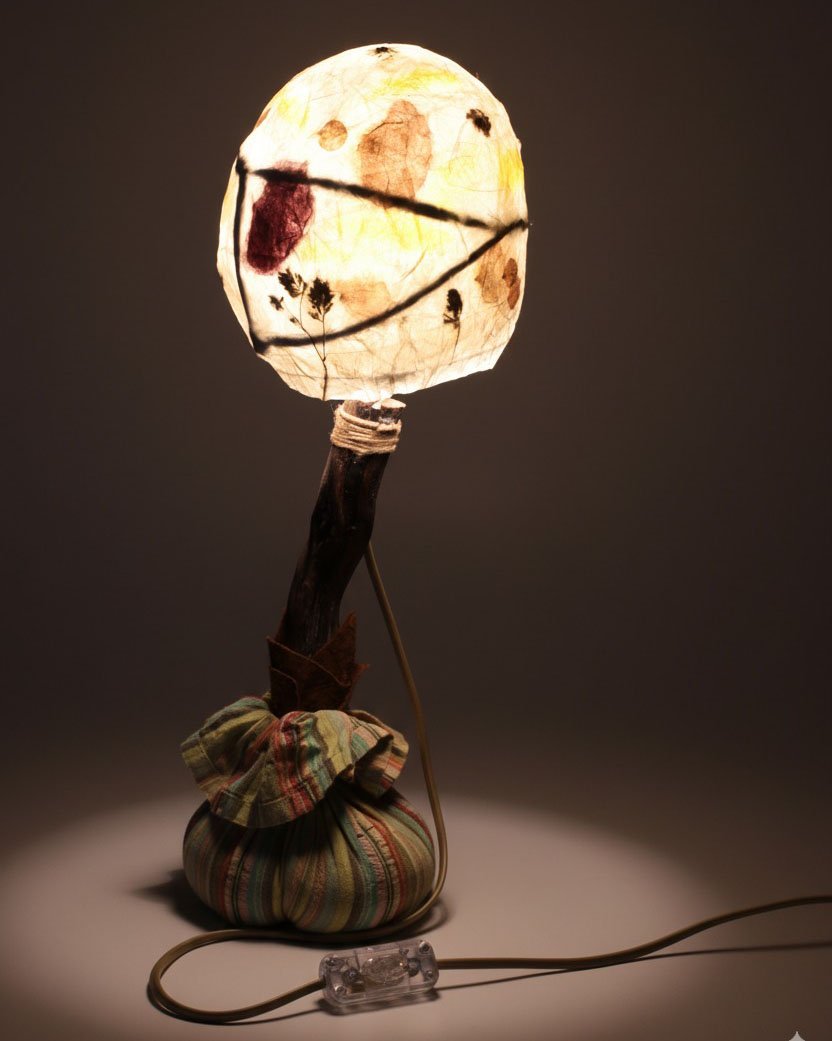 Lámpara de pie con tronco de madera curvado y pantalla esférica iluminada.